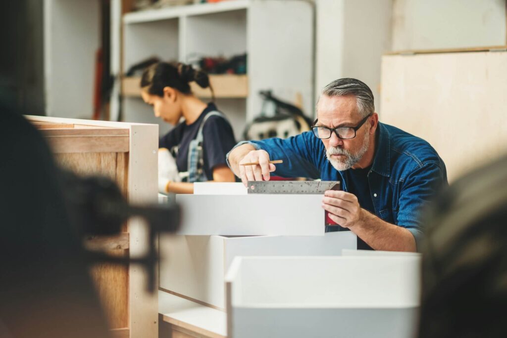 Worker checking finished furniture with a ruler on a workshop floor, representing ISO 9001 quality control