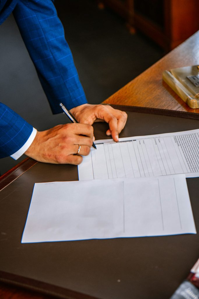 Person in a blue suit signing certification paperwork at a desk